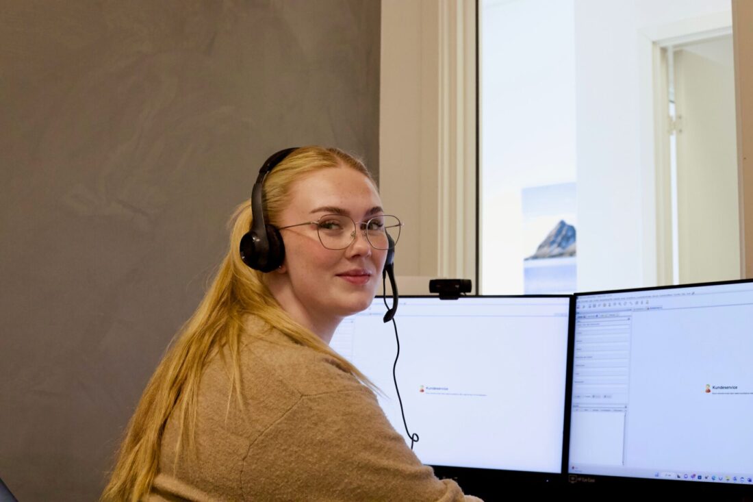 Bilde av dame foran en datamaskin med øretelefoner, som jobber i et kundesenter